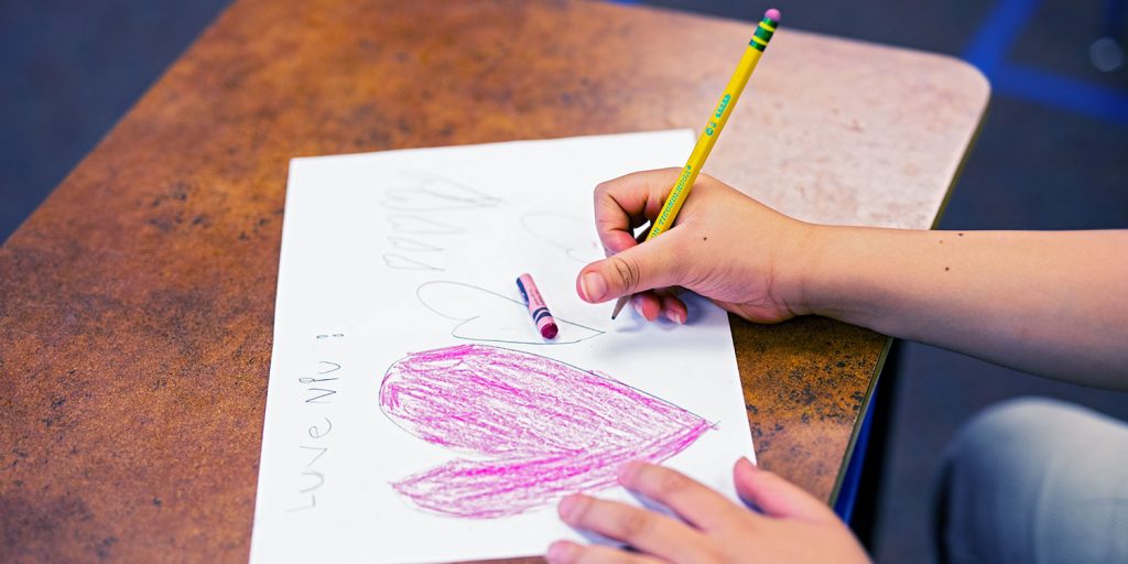 Students hand holding a pencil and drawing a picture with hearts.